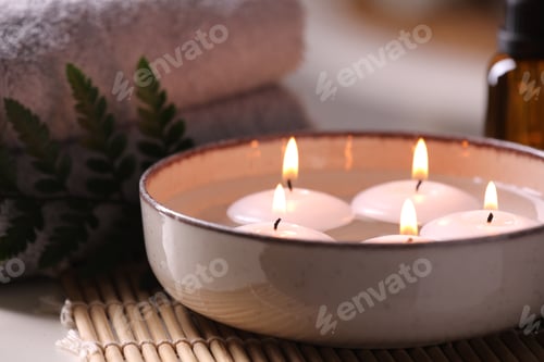 Preview: Spa composition. Burning candles in bowl, towels and fern leaf on table, closeup