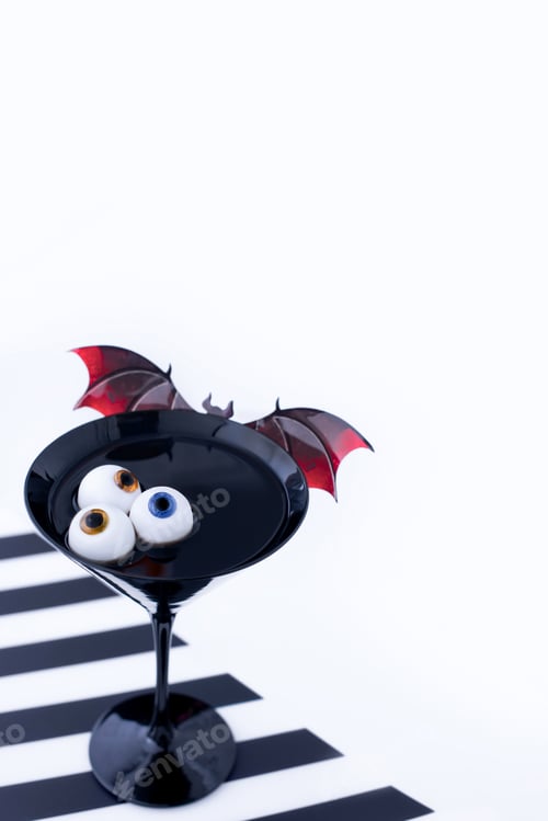 Preview: Halloween cocktail with eyeballs and bat in black martini glass.