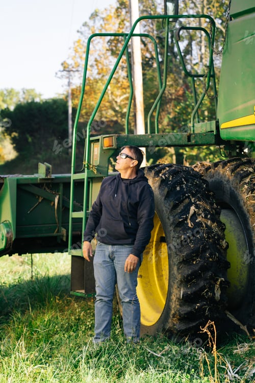 Preview: Adult male standing by a combine looking up at grain or corn loading into the back of a big truck