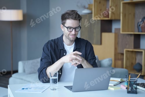 Preview: Young handsome german man wearing glasses working on laptop computer remotely from home