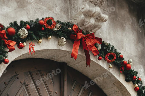Preview: Stylish modern christmas spruce branches with gold ornaments and red bow on old building facade