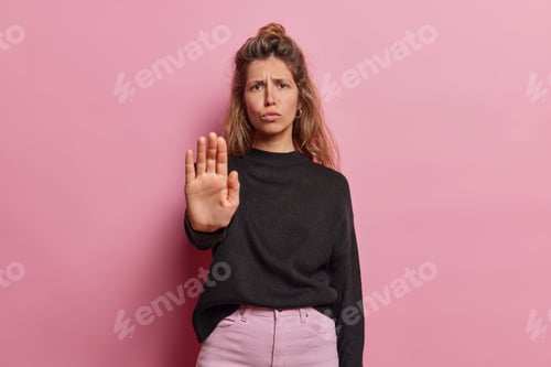 Preview: Studio shot of dissatisfied woman has unhappy expression shows stop gesture with palm of hand
