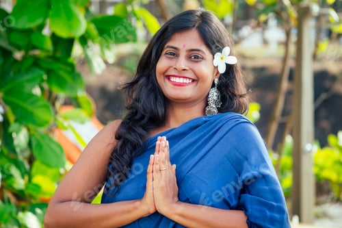 Preview: cheerful young indian woman with white flover in hair relaxing hand gesture namaste on beach in Goa