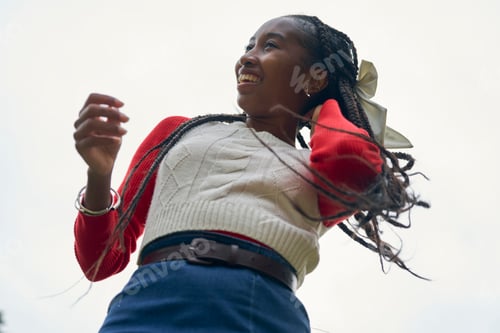 Preview: Woman smiling outdoors with braids and a red sweater, captured from a low angle. Bruges, Belgium