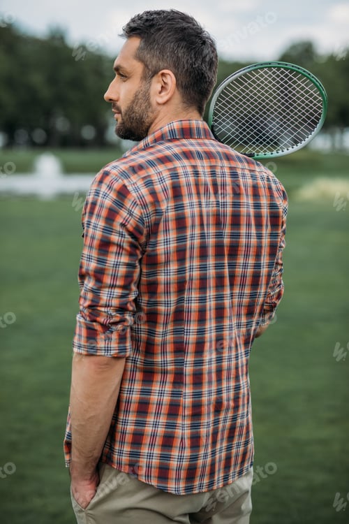 Preview: handsome caucasian man holding badminton racquet and standing on green field