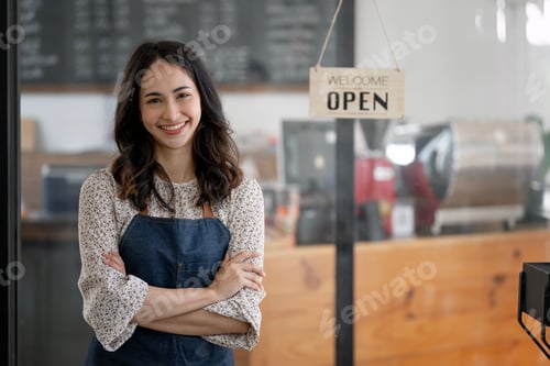 Preview: attractive young beautiful caucasian barista in apron smiling at camera in coffee shop counter.
