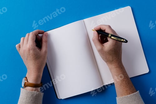 Preview: Hands of caucasian woman holding pen and writing in notebook with copy space on blue background
