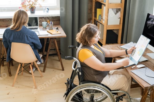 Preview: Young businesswoman in wheelchair looking at paper with charts and diagrams