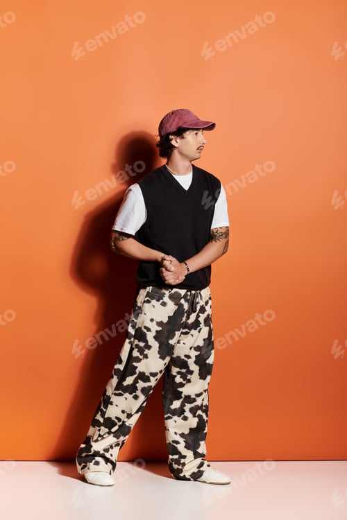 Preview: Stylish young man showcases contemporary fashion against a vibrant orange background