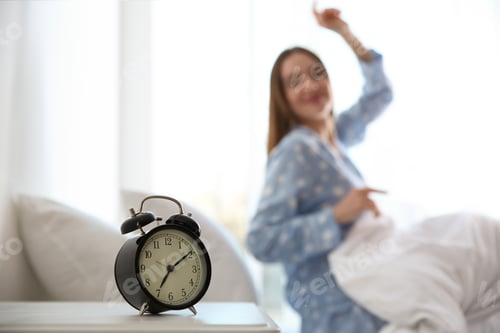 Preview: Young woman stretching at home in morning, focus on alarm clock