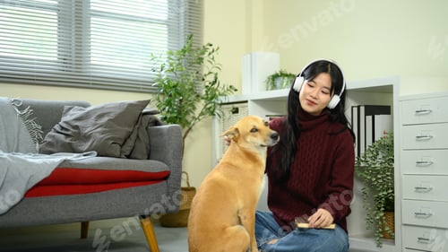 Preview: Young woman wearing headphones sitting on the floor with her dog, enjoying a relaxing moment at home