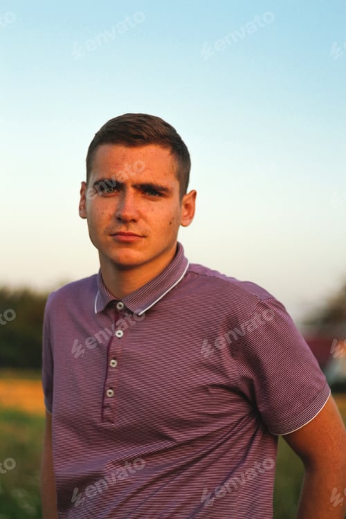Preview: Young man. Portrait of serious young brunette man in purple polo shirt standing outdoor on nature ba