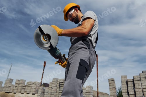 Preview: Posing for a camera with circular saw. Male worker in yellow colored uniform have job with pavement