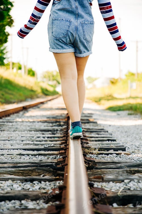 Preview: woman walking on train tracks with short legs on a sunny day