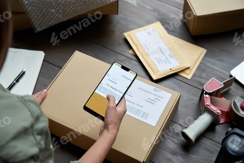 Preview: Female warehouse worker scanning barcode on shipping box on smartphone.