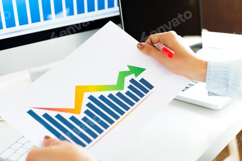 Preview: Person holding report with growth chart next to computer on desk during work hours