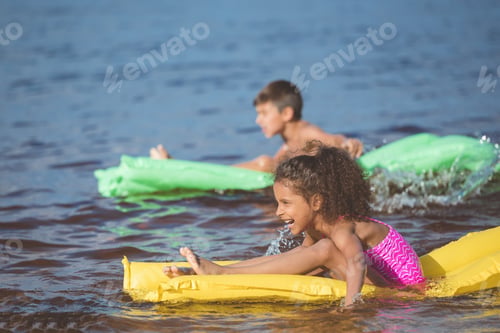 Preview: side view of happy african american girl swimming on inflatable mattress at sea
