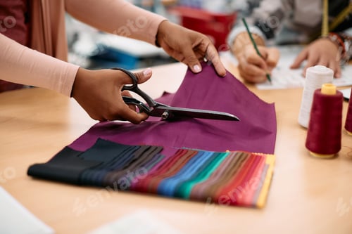 Preview: Close-up of clothing designer cutting textile with scissors at her studio.