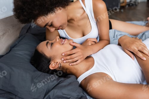 Preview: happy and lesbian african american woman hugging girlfriend on bed