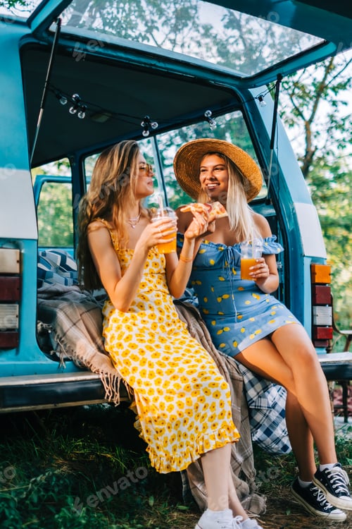 Preview: Two attractive cheerful women drinking lemonade near van and eating pizza