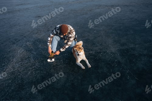 Preview: Cold weather. Man with Akita Inu dog is on the ice with skates in winter