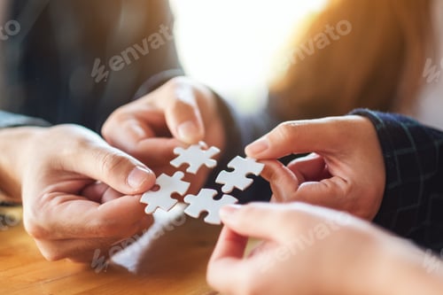 Preview: Closeup image of a group of people holding and putting a piece of white jigsaw puzzle together