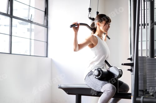 Preview: Asian woman doing back lat pull-down in training gym