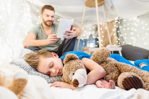 Preview: Smiling father reading book to cute little boy sleeping with teddy bear