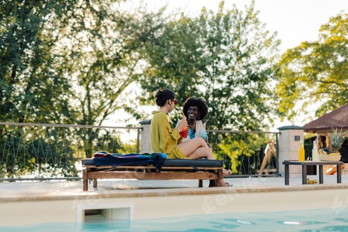 Preview: Two young women relaxing by the pool, enjoying refreshing drinks on a sunny day
