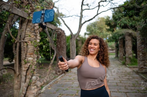 Preview: Smiling woman taking selfie with smartphone in park