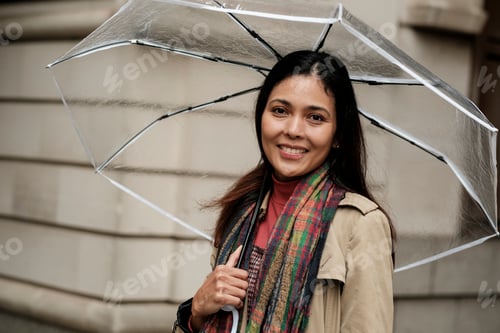Preview: Woman smiling holding clear umbrella on a rainy day