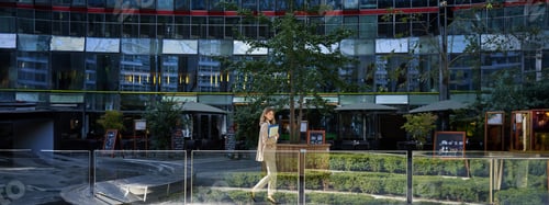 Preview: Silhouette of young business woman in beige suit, walking in city center, posing near office