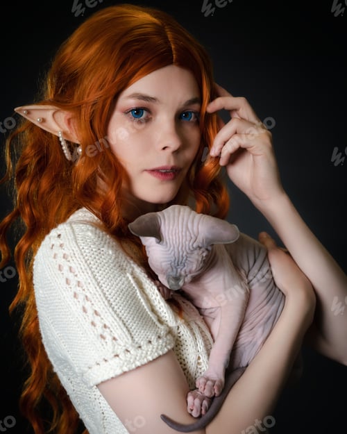 Preview: Young female elf cosplay with sleeping Sphinx kitten in hands. Close-up portrait on black background