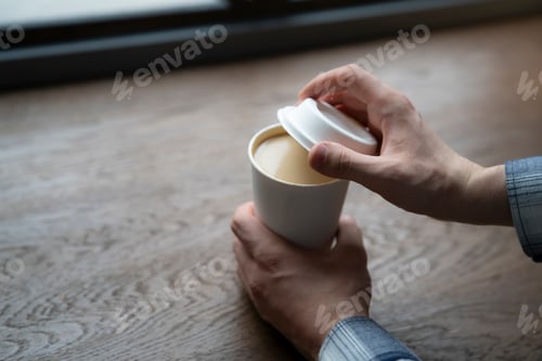 Preview: A close-up view of a persons hands as they remove the cap from a takeaway coffee cup, revealing the