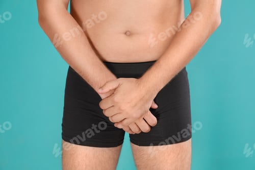 Preview: Man suffering from pain on turquoise background, closeup. Urology problems