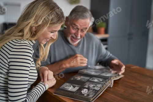 Preview: Caucasian woman looking at old pictures in album with senior dad