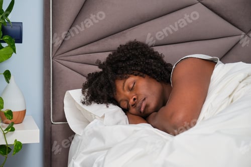 Preview: African young woman sleeping on white sheets in bed.