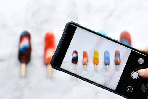 Preview: Influencer using a phone mobile device to take photo of colorful flat lay of popsicles