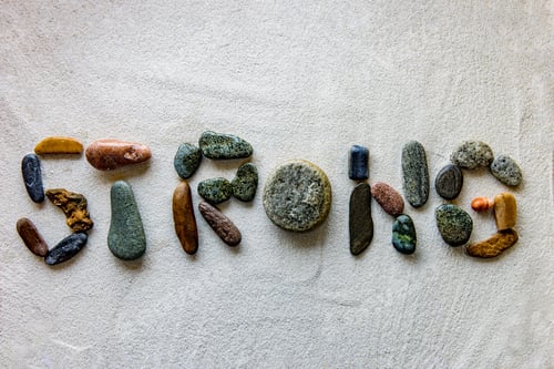 Preview: Word STRONG is written using colored stones on a white sand surface