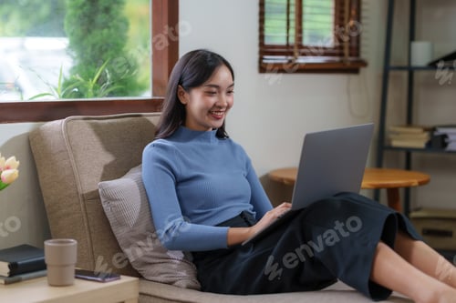 Preview: Cute Asian young woman using laptop computer in the living room, watching movie, listening to music