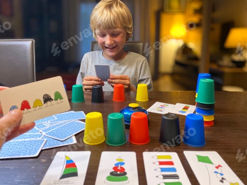 Preview: Game night, blond 9 years old boy playing with mother board game, smiling, cozy dark room with lamps