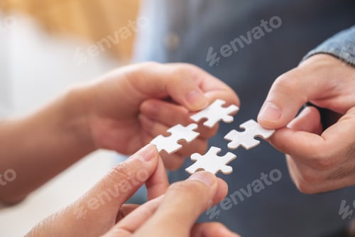 Preview: Closeup image of people's hands holding and putting a piece of white jigsaw puzzle together