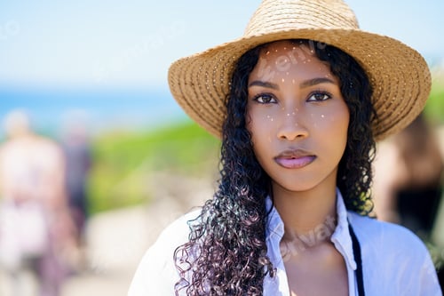 Preview: A young woman wearing a straw hat relaxing by the beach, enjoying a sunny day outdoors