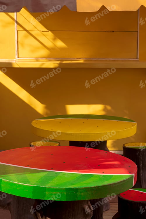 Preview: Decorative stucco garden table in watermelon shape in front of yellow coffee street kiosk