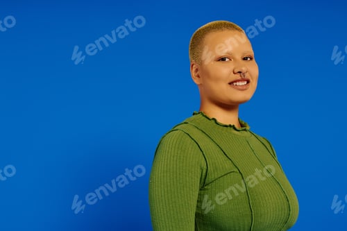 Preview: Stylish young woman with a unique hairstyle poses against a vibrant blue backdrop