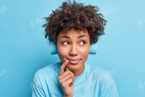 Preview: Close up shot of dreamy Afro American woman smiles gently concentrated thoughtfully aside listens ly