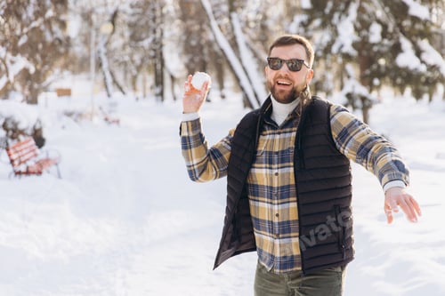 Preview: Smiling man throwing snowball in snowy winter park