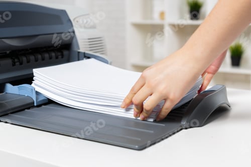 Preview: Hand placing papers into a printer on a desk in a bright office space during the day