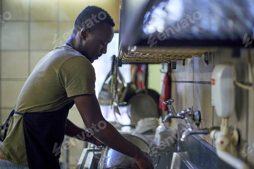 Preview: Young man washing dishes in restaurant kitchen, South Africa