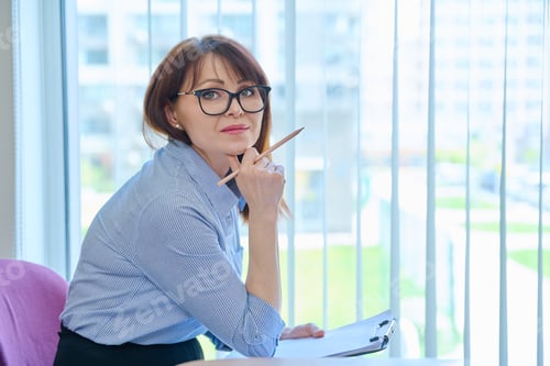 Preview: Middle aged woman with clipboard sitting in office near window.